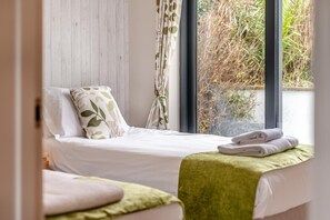 A bedroom with a bed, pillows, a window with curtains, and a view of greenery outside.