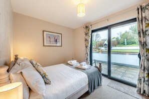 A bedroom with a bed, a bedside table, a lamp, a framed picture on the wall, and a view of the outside through a glass door. - 6 Bed in Woolacombe (oc-mouro) (Woolacombe)