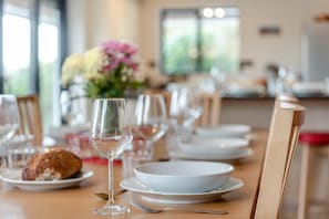 A dining table set with plates, glasses, and cutlery, with a flower arrangement in the background. - 6 Bed in Woolacombe (oc-mouro) (Woolacombe)