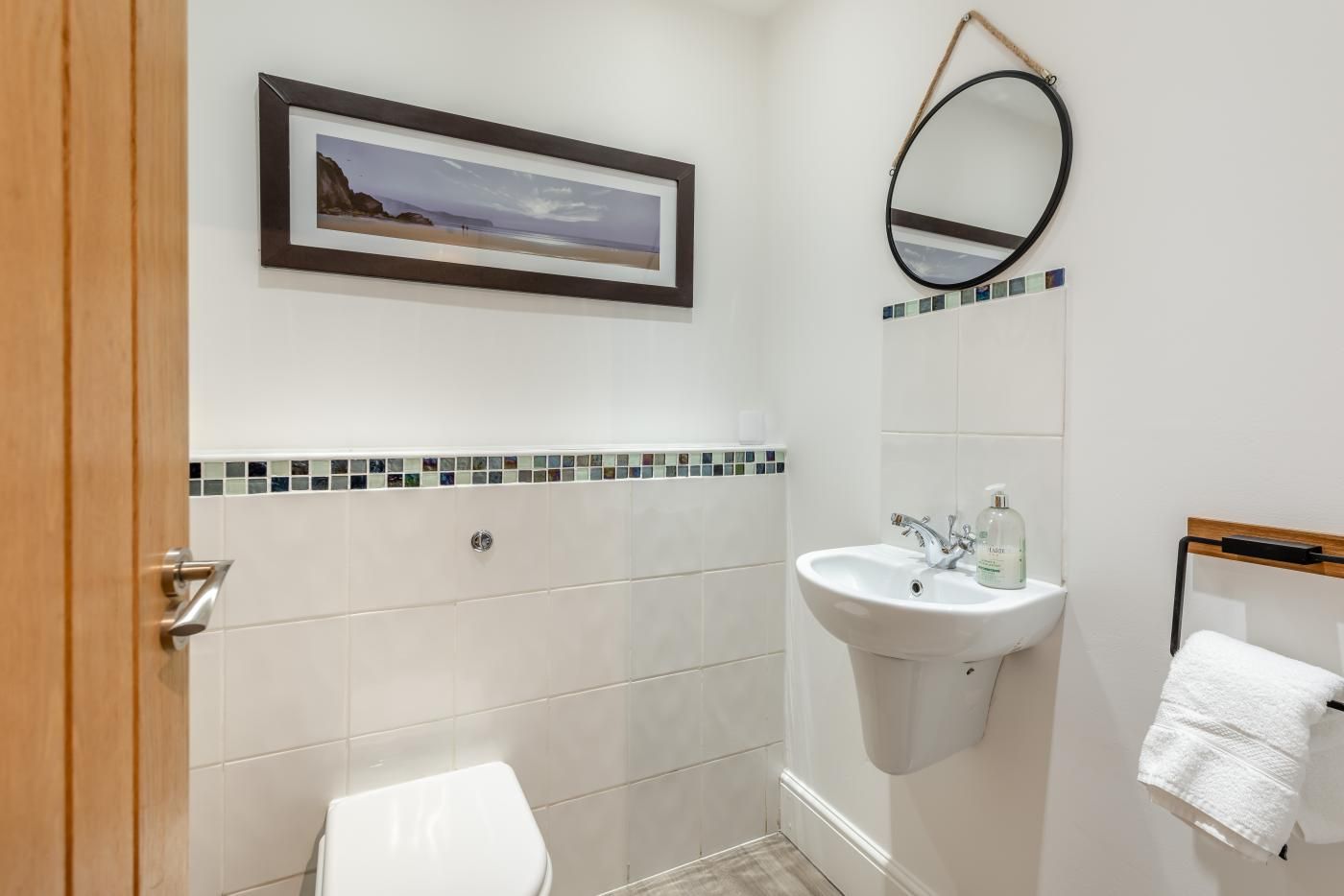 A bathroom with a toilet, sink, mirror, and a framed picture on the wall.