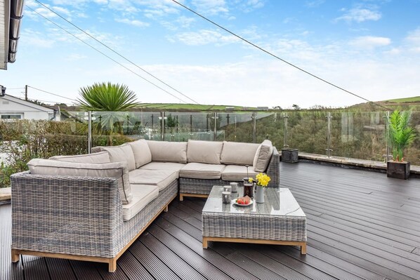 Un espace de détente extérieur moderne, avec un canapé en osier et une table basse en verre, offrant une vue sur un paysage pittoresque.