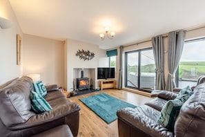 A living room with a fireplace, leather sofas, a flat-screen TV, and a large sliding glass door leading to a balcony.