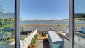 A view from a balcony overlooking a beach with boats, a clear sky, and a wooden deck with outdoor furniture.