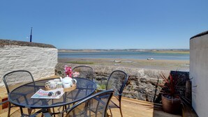 A seaside patio with a table set for two, a chair, a potted plant, and a stone wall.