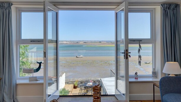 A room with large windows overlooking a beach, a small table with chairs, and a lamp on a windowsill.