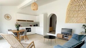 Ein modernes Wohnzimmer mit einem blauen Sofa, einem Esstisch mit Stühlen, einer Küchenzeile und einem Fernseher.