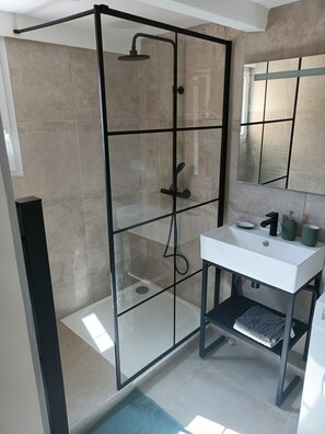 Ein modernes Badezimmer mit einer Duschkabine aus Glas, einem weißen Waschbecken und einem Spiegel darüber.