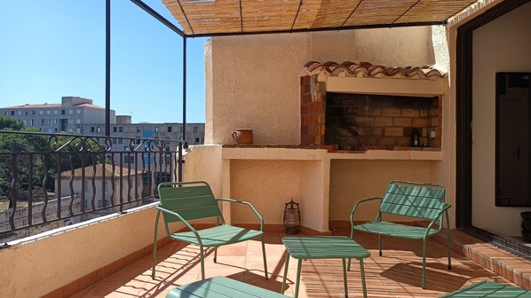 Ein Balkon mit zwei grünen Stühlen, einem kleinen Tisch und einem Backofen aus Ziegeln.