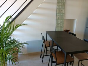 Ein Essbereich mit einem langen Tisch, Stühlen, einer Zimmerpflanze und einer Wand mit Muster.