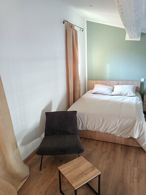 Ein Schlafzimmer mit Bett, Stuhl, kleinem Tisch und Vorhang.