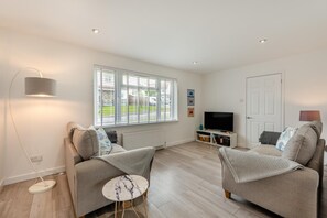 A modern living room with two sofas, a TV stand, a floor lamp, and a window with blinds.