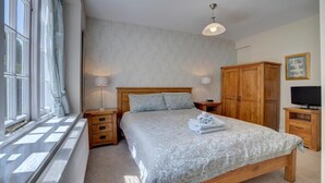 A bedroom with a bed, wooden wardrobe, bedside lamps, a radiator, and a television. - 4 Bed in Lynmouth (oc-marins) (Barbrook)