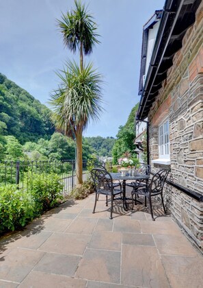A patio with a table and chairs, a stone wall, and a view of a lush green hillside.