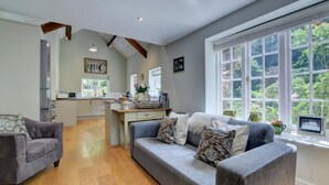 A spacious living area with a grey sofa and armchairs, a wooden floor, and a kitchen in the background. - 4 Bed in Lynmouth (oc-marins) (Barbrook)
