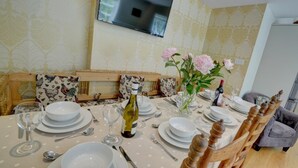 A dining area with a table set for four, chairs, a television mounted on the wall, and a vase with flowers. - 4 Bed in Lynmouth (oc-marins) (Barbrook)