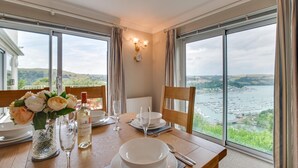 Une table à manger dressée pour deux personnes, avec vue sur une baie et des collines.
