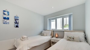 Une chambre avec deux lits, une table de chevet, une lampe et une fenêtre avec des rideaux.