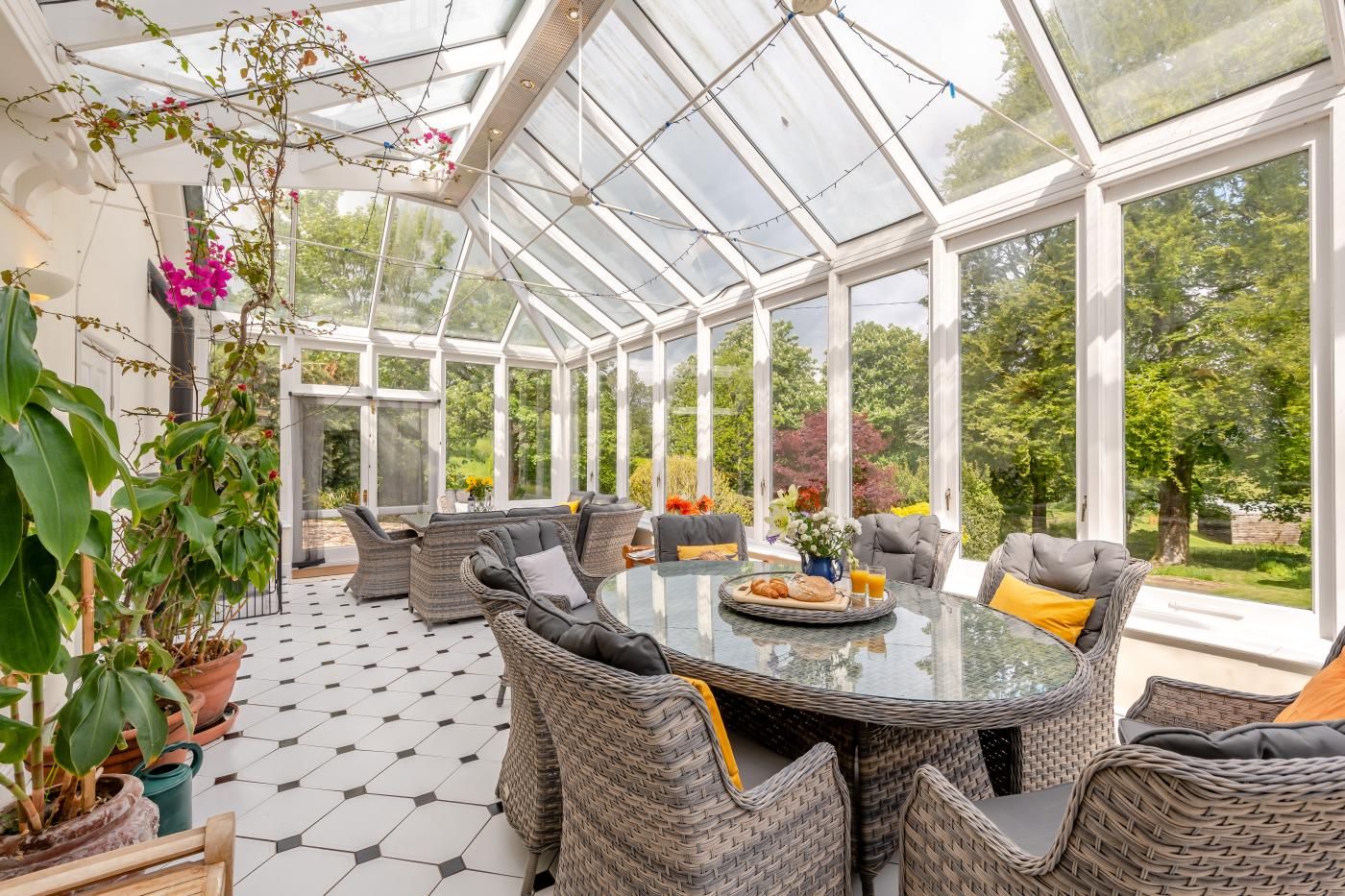 A conservatory with wicker furniture, a glass table, and a view of the garden.