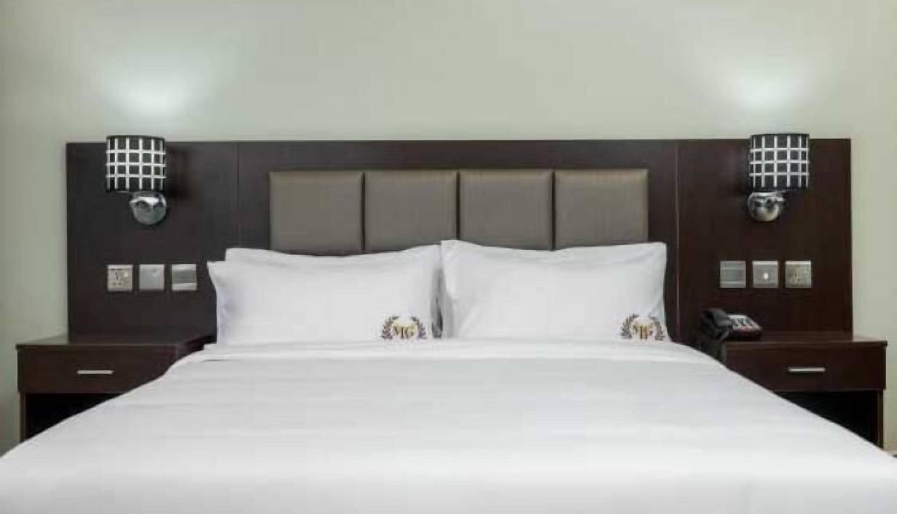 A hotel room with a large bed, two bedside tables, and a headboard with built-in lighting.