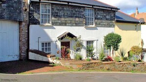 A two-story house with a stone facade, a white front door, and a small porch with plants.