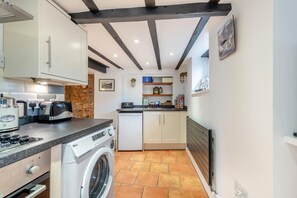 A compact kitchen with a washing machine, a stove, and a small dining area. - 3 Bed in Torquay (oc-h75059) (Torquay)
