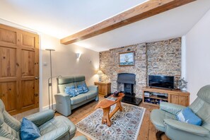 A cozy living room with a stone wall, a fireplace, a television, and comfortable seating. - 3 Bed in Torquay (oc-h75059) (Torquay)