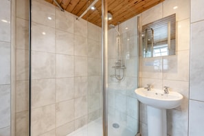 A modern bathroom with a glass-enclosed shower, a white sink, and a wooden ceiling.