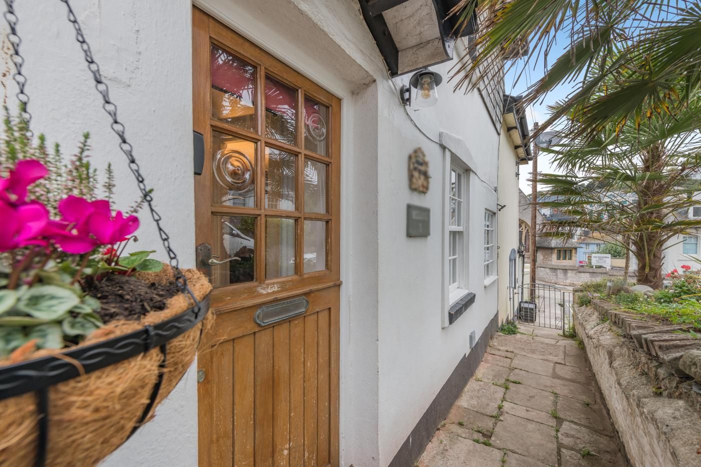 A white building with a wooden door and windows, a hanging flower basket, and a stone pathway.