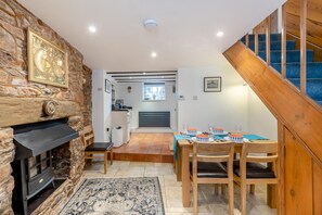 A cozy dining area with a wooden table set for four, a stone fireplace, and a staircase leading to an upper level. - 3 Bed in Torquay (oc-h75059) (Torquay)