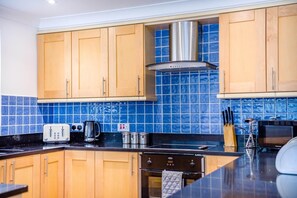 A kitchen with wooden cabinets, a stainless steel range hood, a black countertop, a toaster, a kettle, and a microwave.