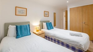 Quarto de hotel com duas camas, um guarda-roupa de madeira e uma mesa de cabeceira com abajur.