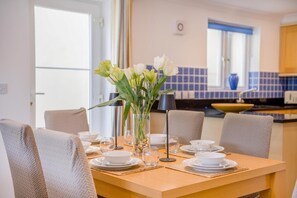 Ein Essbereich mit Tisch für vier Personen, einem Blumenstrauß und Blick auf die Küche im Hintergrund.