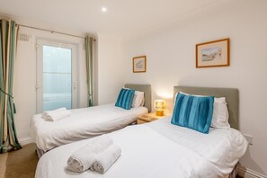 A hotel room with two beds, a window with curtains, and a nightstand with a lamp.