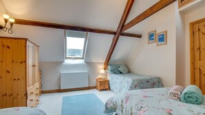 A bedroom with a sloped ceiling, wooden beams, a window, a radiator, a bed with floral bedding, a nightstand, and a wardrobe. - 2 Bed in Exminster (oc-h28725) (Exminster)
