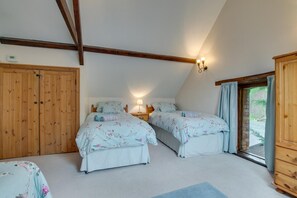 A bedroom with two beds, a wooden wardrobe, a nightstand, and a window with curtains.