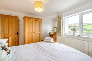 A bedroom with a bed, wooden wardrobe, dresser, window with view, and a hanging light fixture. - 4 Bed in Frogmore (oc-bc721) (Frogmore)