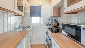 Een compacte keuken met witte kastjes, een RVS-gootsteen, een kookplaat en een vaatwasser.
