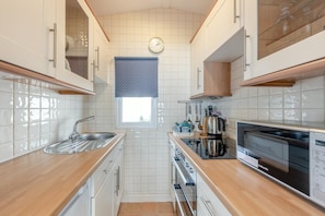 A compact kitchen with white cabinets, a stainless steel sink, a stove, and a dishwasher.