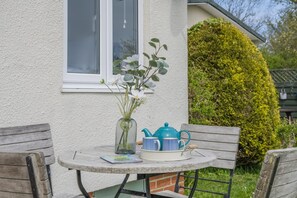 A small round table with a vase of flowers, a teapot, and a cup on a patio.