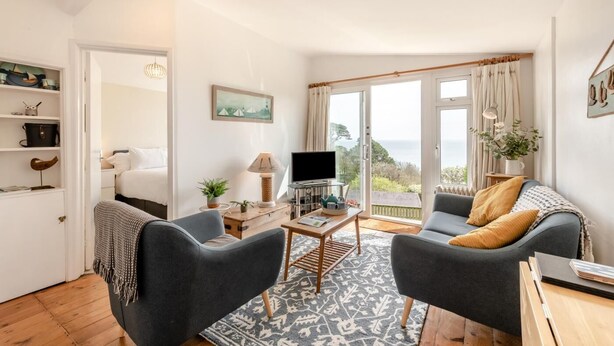Een woonkamer met een bank, fauteuil, televisie en uitzicht op zee.