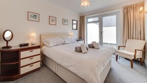 Ein Hotelzimmer mit Bett, Nachttisch mit Lampe, Stuhl, Schreibtisch mit Spiegel und Fenster mit Vorhängen.