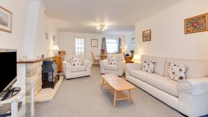 Ein Wohnzimmer mit einer Couch, Sesseln, einem Couchtisch, einem Kamin und einem Fernseher.