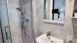 Ett modernt badrum med en dusch som är avskärmad med glasväggar, en vit tvättställ och en spegel ovanför.