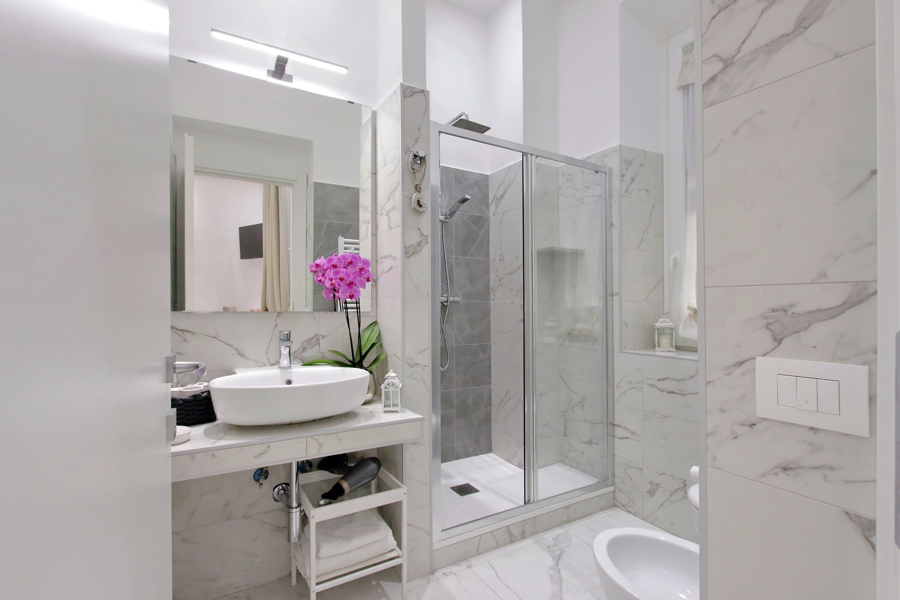 Une salle de bain moderne avec un lavabo blanc, un miroir et une douche en verre.