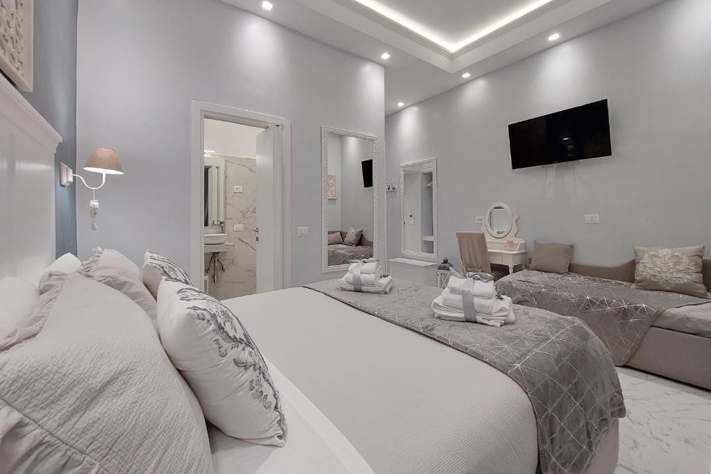 A modern bedroom with a large bed, two smaller beds, a TV, and a mirror.