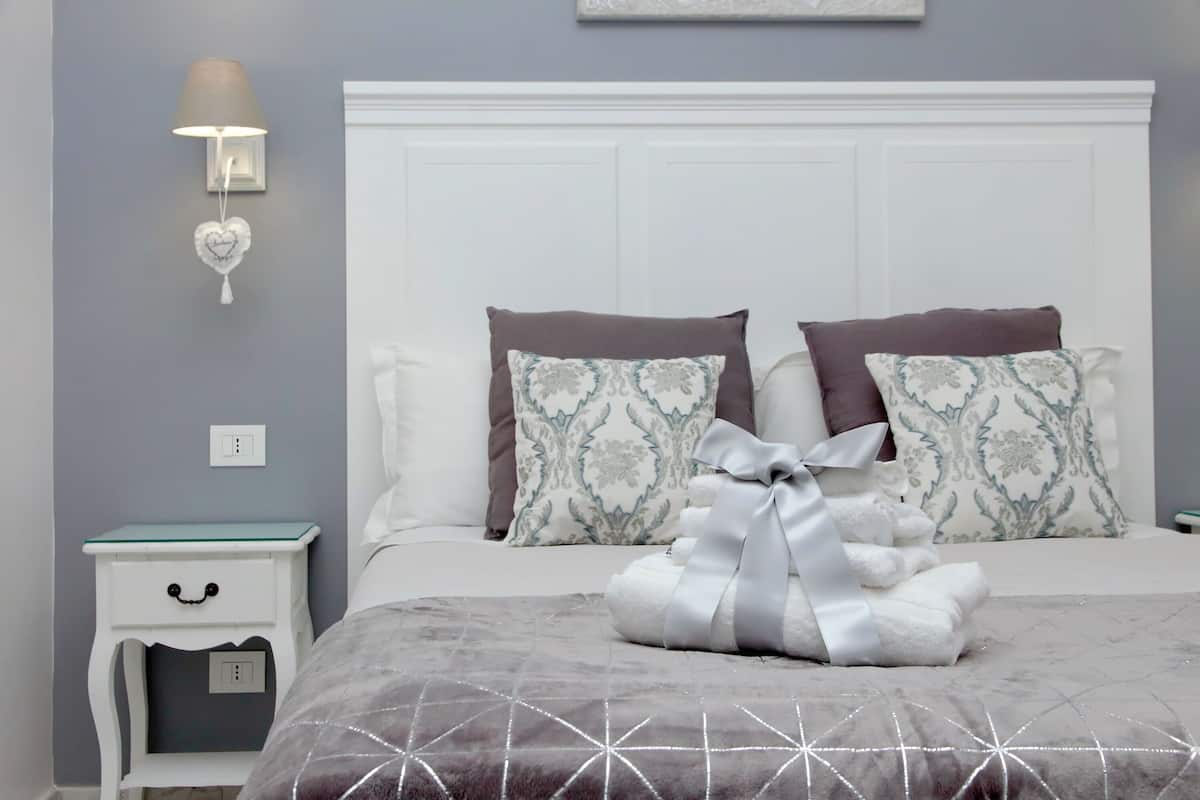Un dormitorio ordenado con cama, almohadas, lámpara de noche y mesita de noche.