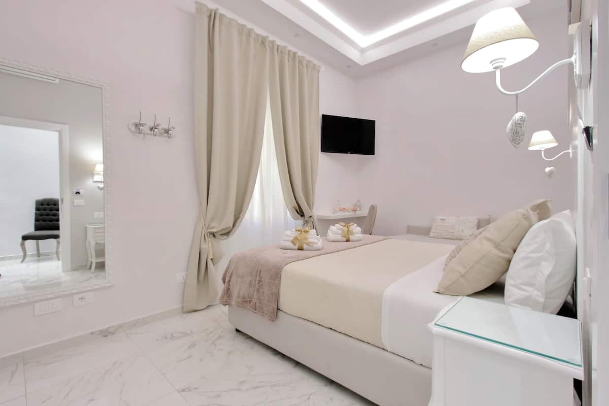 Un dormitorio moderno con una cama grande, una mesita de noche, un espejo y un televisor fijado a la pared.