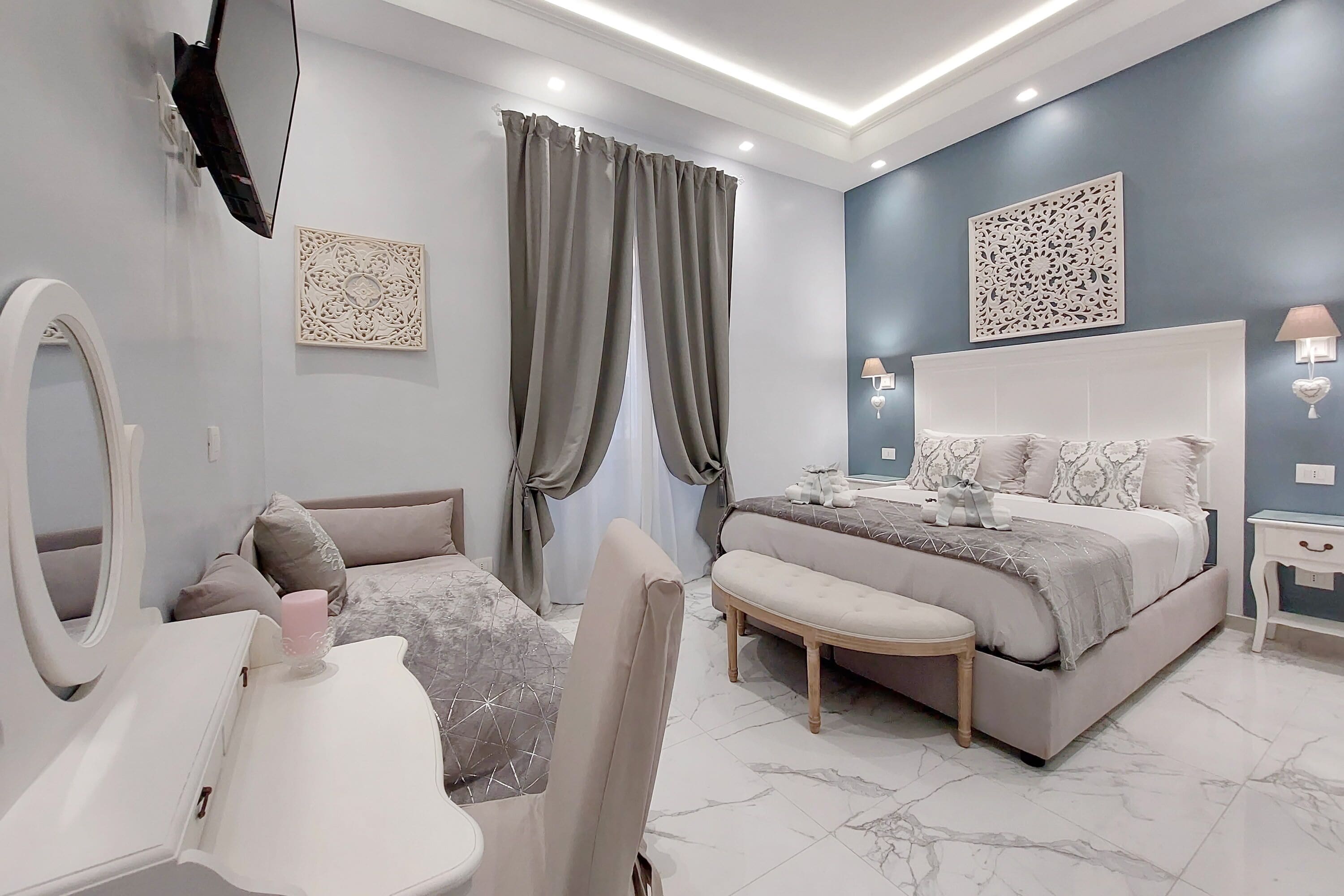 A modern bedroom with a large bed, bedside tables, a vanity with a mirror, and a TV mounted on the wall.
