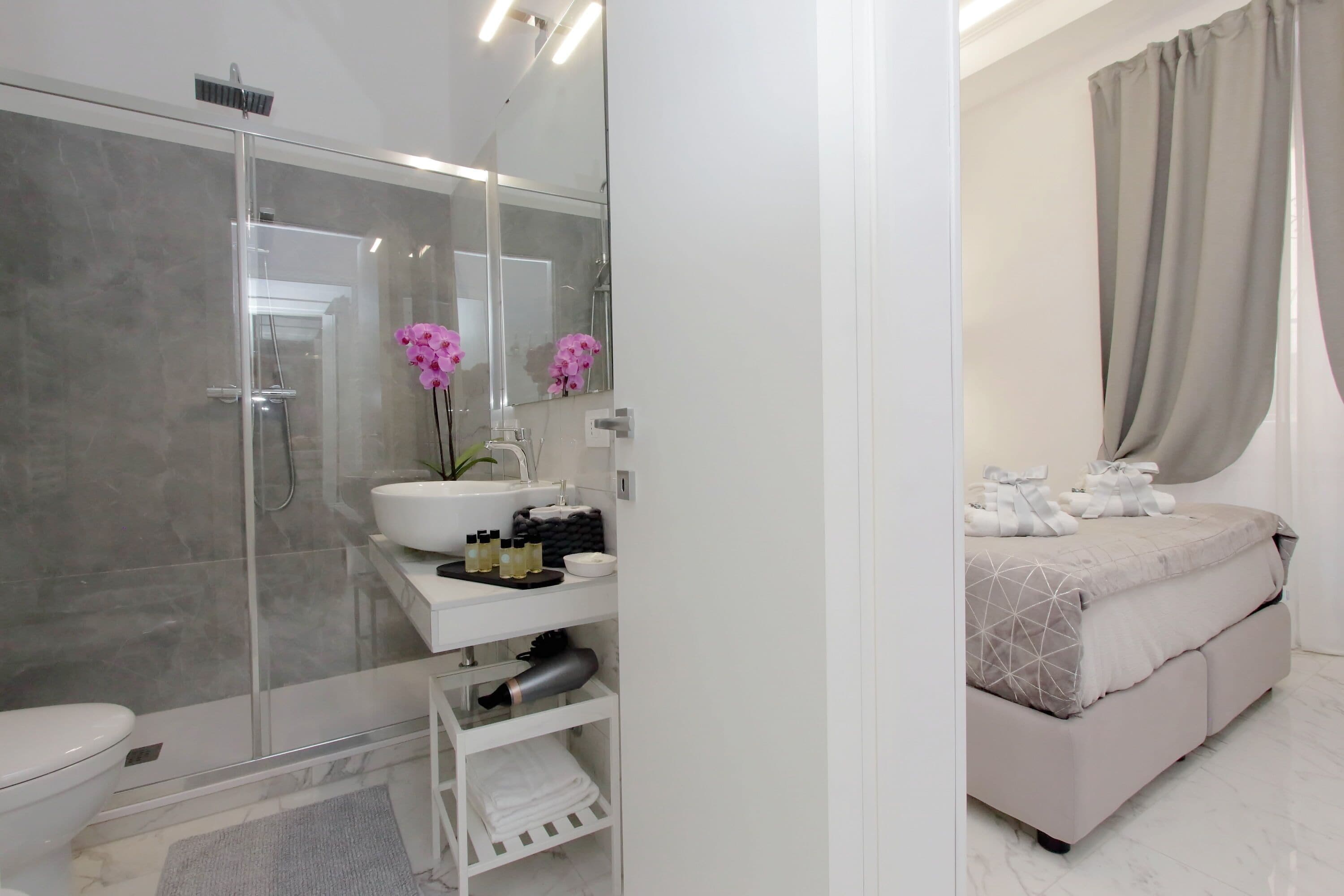 A modern bathroom with a glass-enclosed shower, a white sink with a mirror, and a vanity with toiletries.