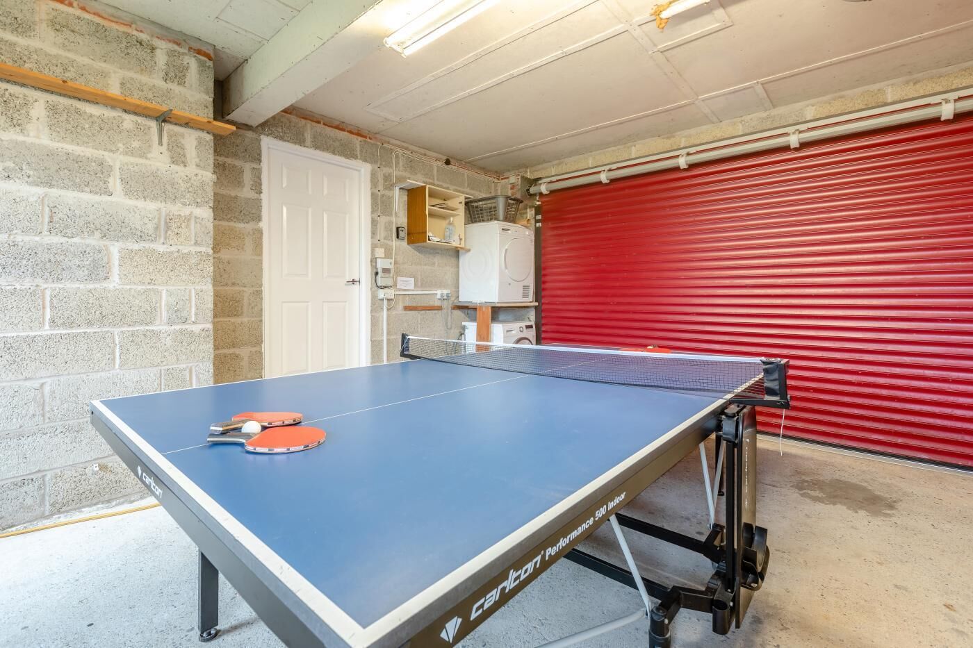 A ping pong table with a white door and a red garage door in the background.